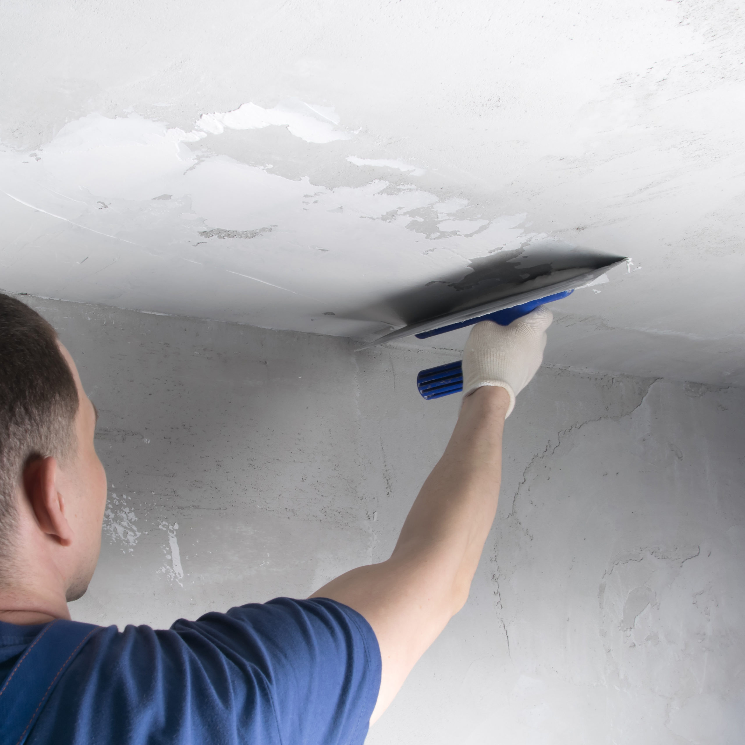 master in a blue uniform, applying the finishing putty on the ceiling, close-up