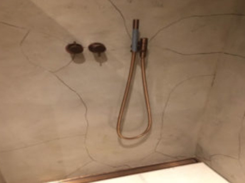 A plaster in a shower's walls is covered by cracks starting from the faucet handles